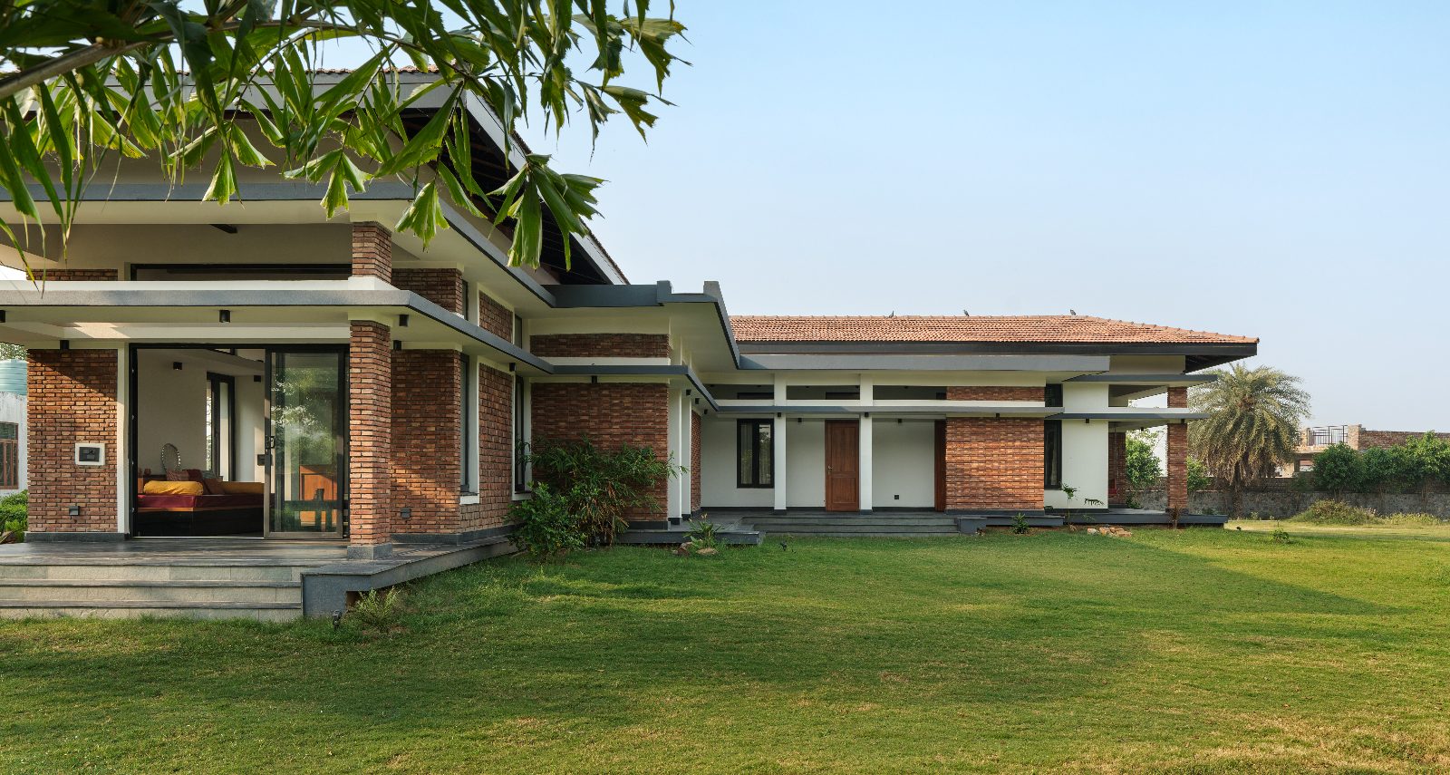 Single-storey brick farmhouse with a terracotta tiled roof, deep eaves and a wide verandah opening onto a large green lawn.