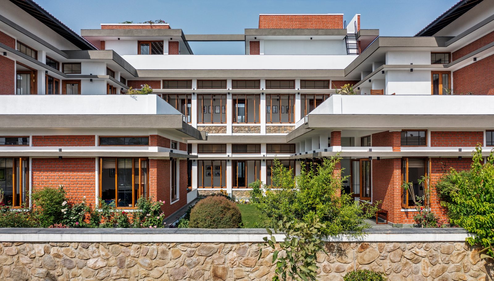 Three-storey brick and white house with deep horizontal overhangs and teak windows, wrapped around a central garden courtyard.